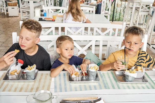 Brothers eat French fries and nuggets from metal utensils together in resort cafe