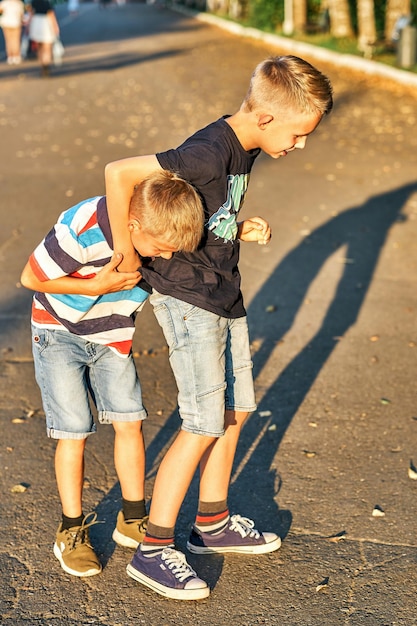 Brothers wrestle on sidewalk in public park Schoolboys have fun in public park in summer evening