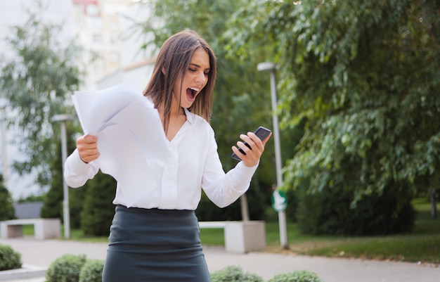 Brought to hysteria, angry business woman dressed in a white blouse and a skirt screams in the phone