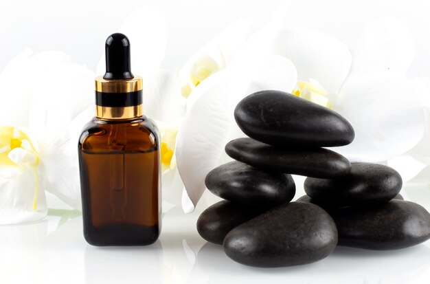 A brown bottle of cosmetic oil stands on a black stone with beautiful orchids Spa concept