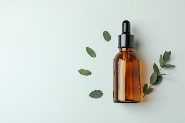 Brown bottle of eucalyptus oil and twig on white background