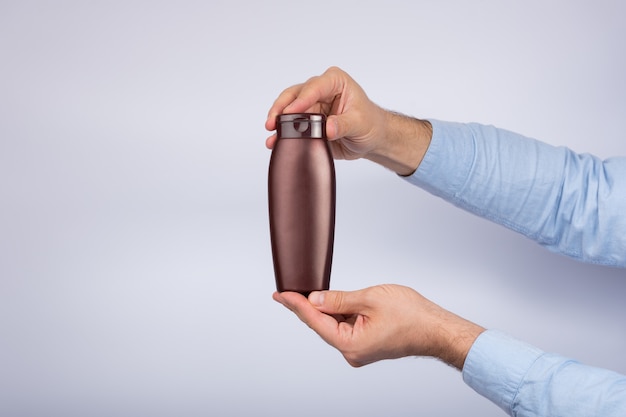 Brown bottle of shampoo or lotion in male hand on white