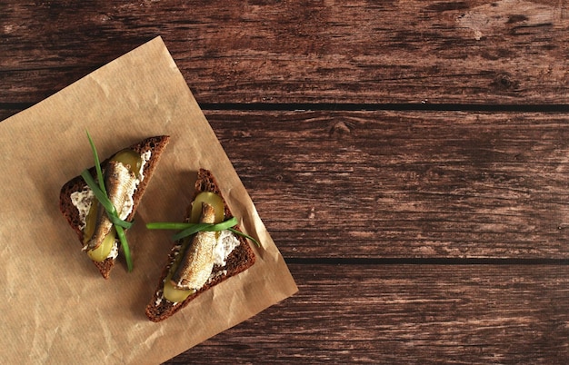 Brown bread sandwiches with pickles onions garlic and sprats on a wooden background