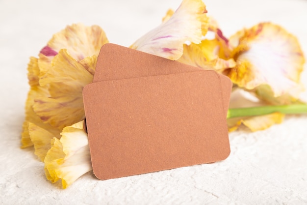 brown business card with iris yellow flowers on white concrete background. side view, copy space