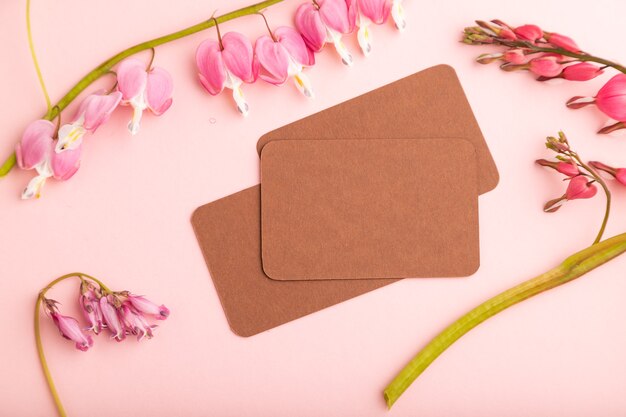 brown business card with pink dicentra, broken heart flowers on pink pastel background. top view