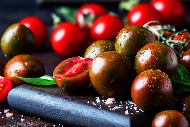 Brown cherry tomatoes with sea salt and green basil on dark table autumn harvest selective focus