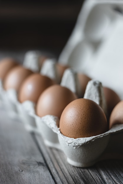 Brown chicken eggs in a carton on wooden surface.