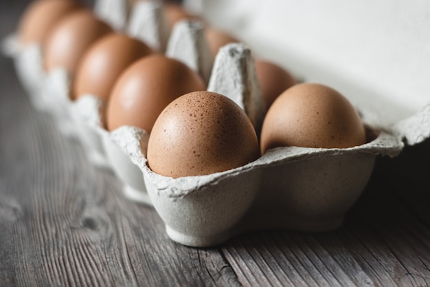 Brown chicken eggs in a carton on wooden surface.