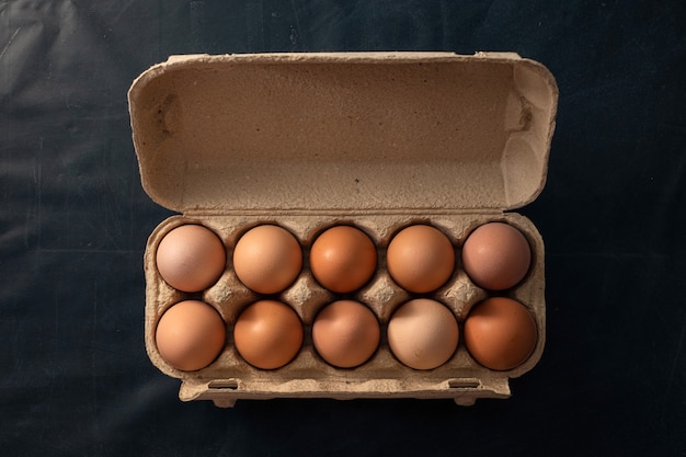 Brown chicken eggs in an open egg carton isolated on black table.