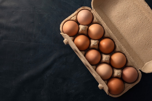 Brown chicken eggs in an open egg carton isolated on black table.