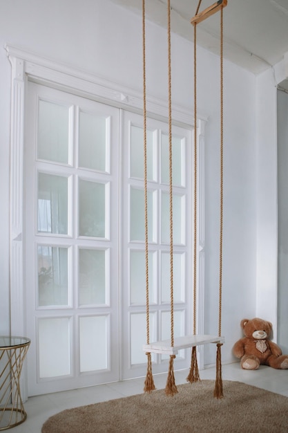 Brown children's swing in a white spacious studio Long glass doors on the background