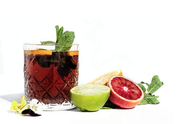 Brown cocktail with citrus blackberry and mint bubbles in a glass white background