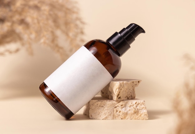 Brown cosmetic bottle with blank label on stones near pampas grass close up Mockup