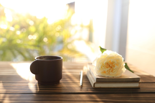 Brown cup and rose and notebooks on wooden table