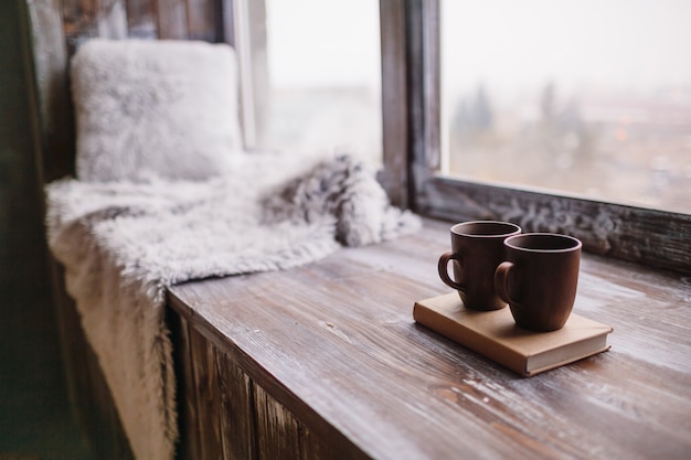 Brown cups stand on a book on wooden windowsill