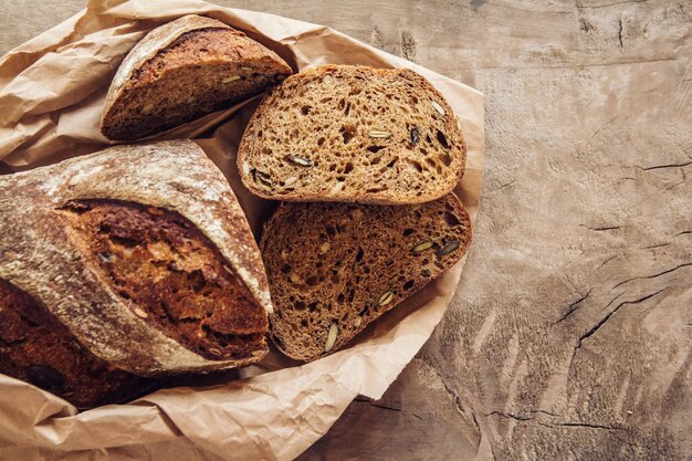 Brown fresh bread with seeds are cut into pieces on old wood background. Top view, copy space