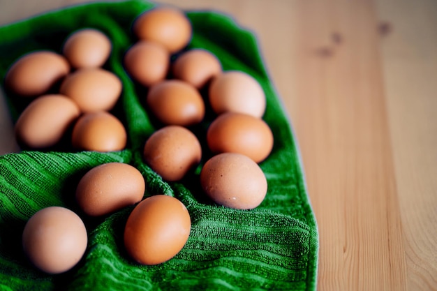 Brown fresh chicken eggs on green kitchen towel on wooden table. Concept of farm products, natural food, healthy eating, easter. Vertical shot.