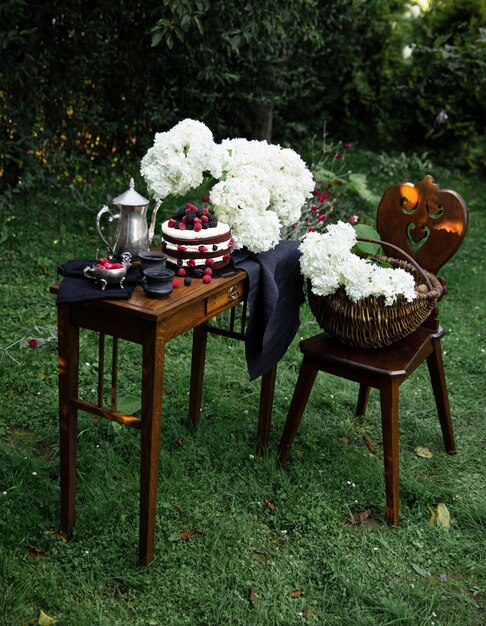 Brown fruit cake on the wooden narrow table in the garden. Silver tea pot and two black cups of tea are complementing the composition. 