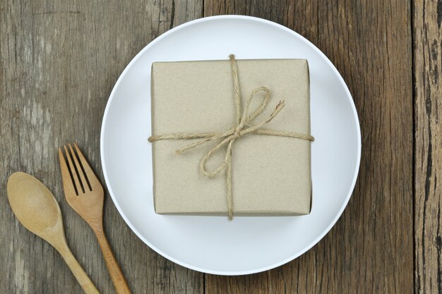 Brown Gift Box in white dish on wooden floor and have wooden spoon.