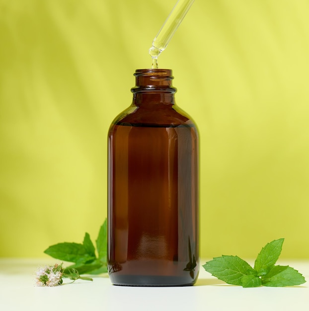 Brown glass bottle with a cosmetic product and a pipette with a drop green background