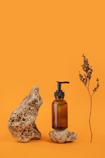 Brown glass bottle with cosmetic product on stone and dried flowers on orange background. Natural Organic Spa Cosmetic concept Front view.