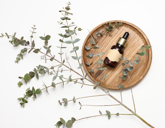 Brown glass bottle with a pipette and an empty glued label on a wooden board next to a branch of eucalyptus