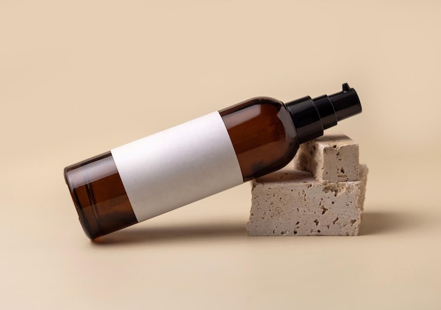 Brown glass cosmetic bottle lies on beige stones on light yellow Mockup