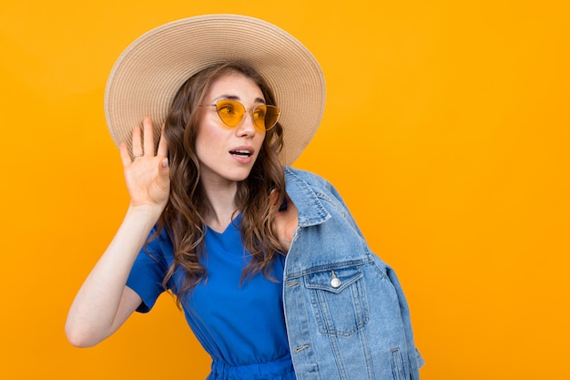 Brown-haired woman in a blue dress on a yellow surface eavesdrops on a conversation