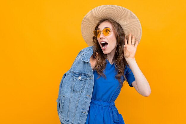 Brown-haired woman in a hat and jeans holds a hand near the ear