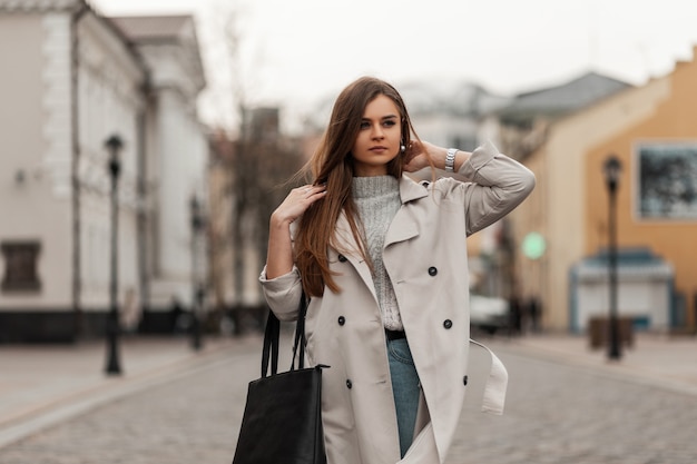 brown-haired woman in spring clothes and sneakers with a leather bag posing along the street