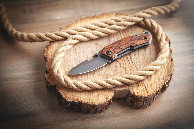 Photo brown knife rope and slice of a tree on wooden background