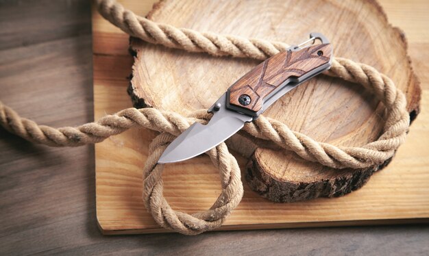 Photo brown knife, rope and slice of a tree on wooden background.