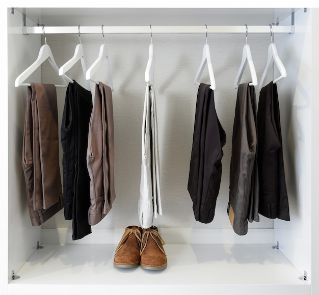 Brown leather shoes and row of black pants hangs in wardrobe