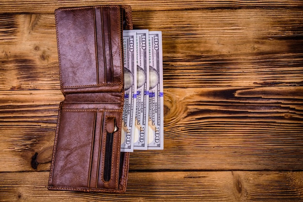 Brown leather wallet and one hundred dollar banknotes on the wooden background Top view