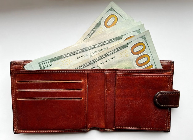 Brown leather wallet with 100 bills in close-up on a white isolated background. American currency