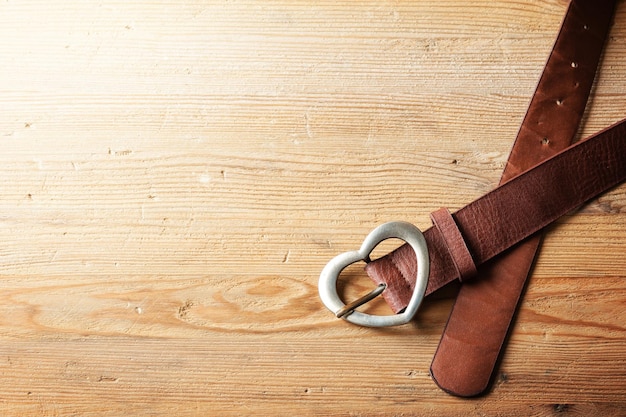 Brown leather woman belt with metal heart shaped belt buckle on wooden board