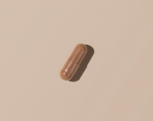 Brown Medical capsule on light beige top view hard shadows Taking dietary supplements