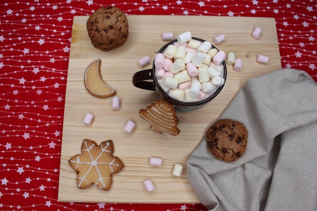 Brown mug with marshmallows Christmas chocolate cookies Gray kitchen rag wood and red tablecloth