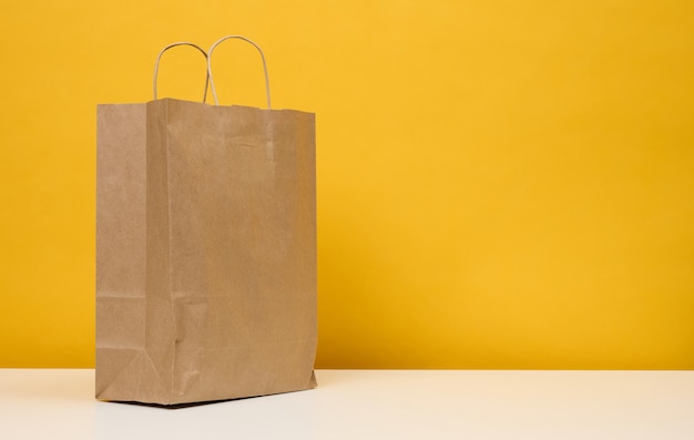 A brown paper bag stands on a white table yellow background