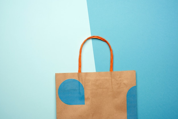 Photo brown paper bag with handles for shopping on a blue background, flat lay