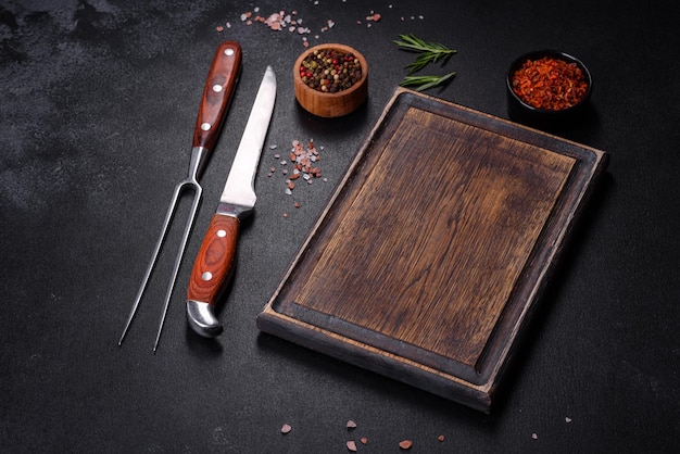 Brown rectangular wooden cutting board with salt and spices on a dark concrete background Cooking at home