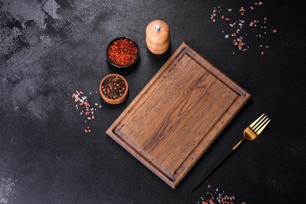 Brown rectangular wooden cutting board with salt and spices on a dark concrete background Cooking at home