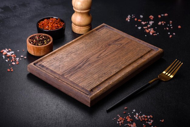 Brown rectangular wooden cutting board with salt and spices on a dark concrete background