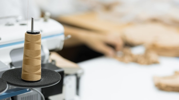 Brown sewing thread skein on spool with blurred fabric background