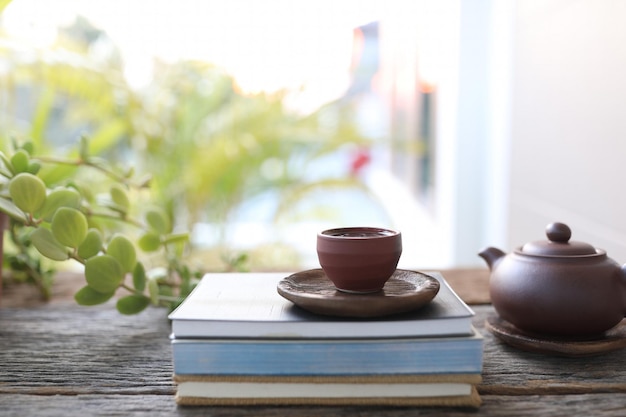 Brown teapot and tea cup and books on wooden table