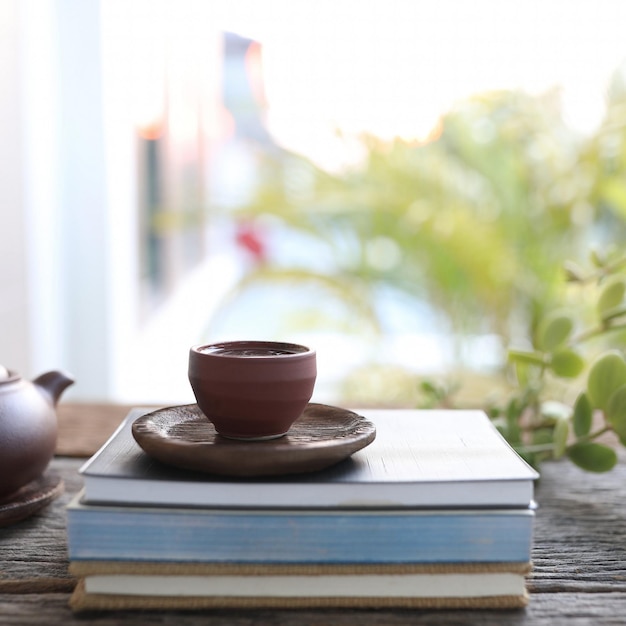 Brown teapot and tea cup and books on wooden table