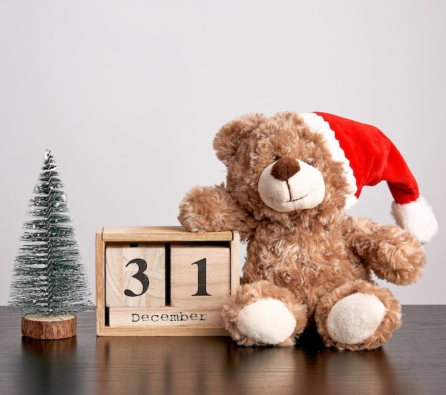 Brown teddy bear in red hat, desk wooden calendar with the date december 31