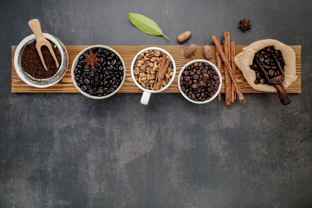 Brown unroasted and dark roasted coffee beans in coffee cup with scoops setup on dark stone.