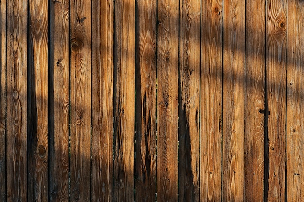 Brown wooden fence texture with shadows in evening sunlight Background of wooden planks