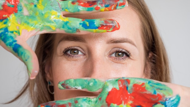 Brownhaired woman shows hands in bright paints posing